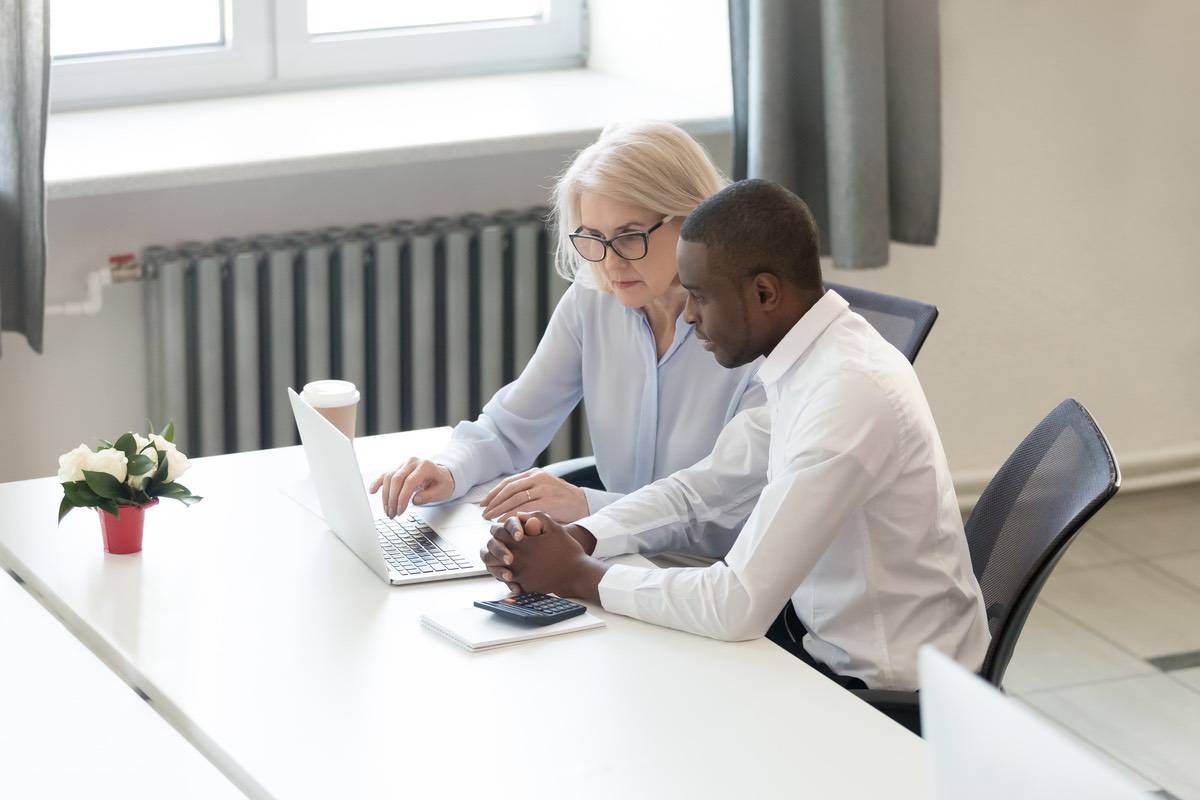 An older woman sits next to a younger man, both are looking at a laptop screen.