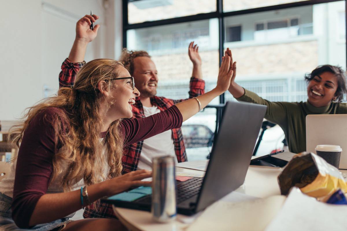 A group of people sitting at an office conference desk smile and give each high fives.