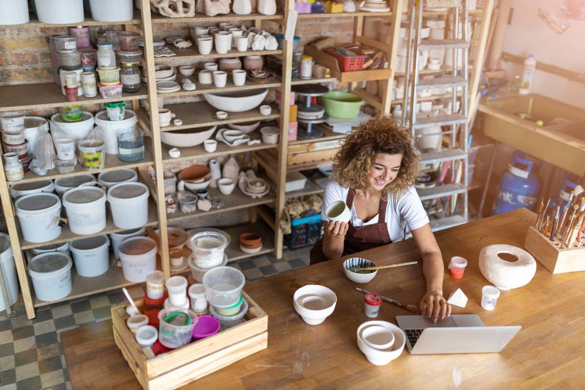 Interior of a shop with pots and a woman wearing an apron stands at the counter busy working