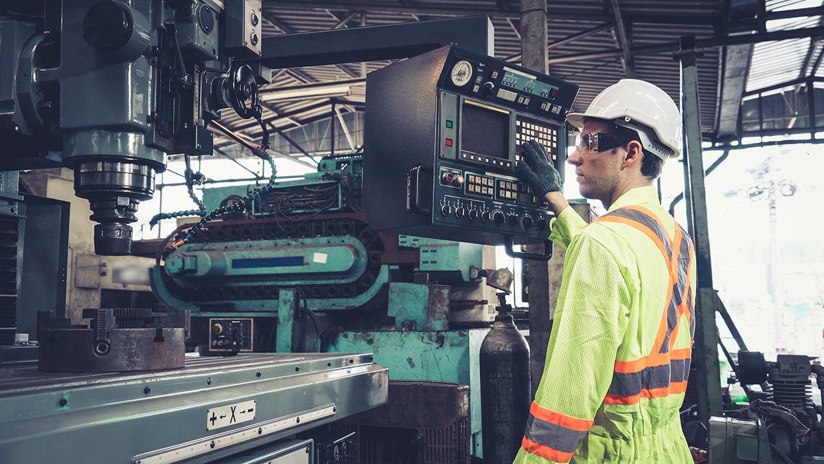 A man in a white hard hat looks over a machine